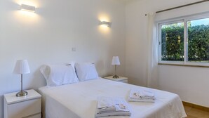 A hotel room with a neatly made bed, two bedside lamps, and a window with a view of greenery. - FLH Praia da Luz Apartment with Pool (Lagos)