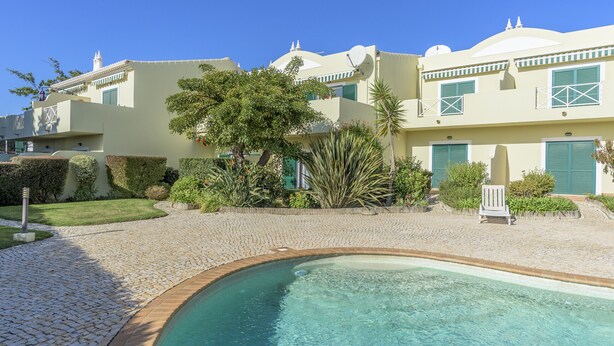 A pool area with a clear blue pool, a paved walkway, and a building with a dome and satellite dish. - FLH Praia da Luz Apartment with Pool (Lagos)