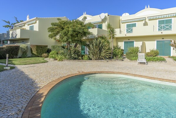 A pool area with a clear blue pool, a paved walkway, and a building with a dome and satellite dish.