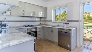 A modern kitchen with white cabinets, a built-in oven, a dishwasher, and a window providing a view of the outdoors. - FLH Praia da Luz Apartment with Pool (Lagos)