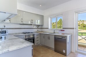 A modern kitchen with white cabinets, a built-in oven, a dishwasher, and a window providing a view of the outdoors.