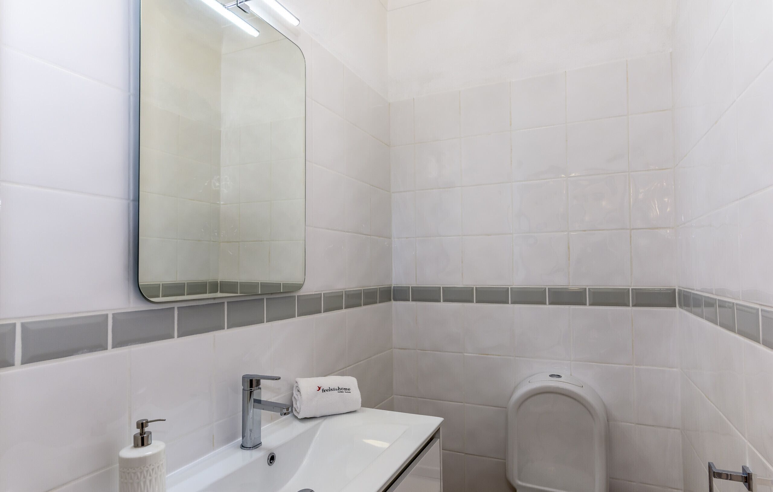 A bathroom with white tiles, a sink, a mirror, and a towel rack.