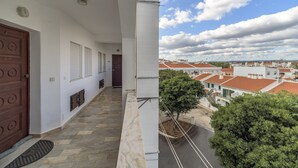 Un balcón con suelo de piedra, una puerta de madera y vistas a un barrio residencial con casas de tejados rojos.