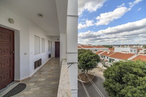 A balcony with a stone floor, a wooden door, and a view of a residential area with red-roofed houses.