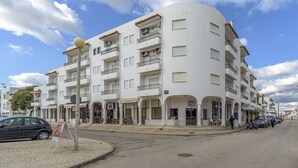 Un edificio blanco de varios pisos con balcones, tiendas y una calle adoquinada.
