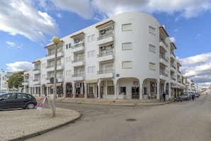 Un immeuble blanc à plusieurs étages, doté de balcons, de devantures de magasins et situé le long d’une rue pavée.