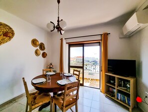 Un coin repas avec une table dressée pour quatre personnes, un ventilateur de plafond et une bibliothèque remplie de livres.