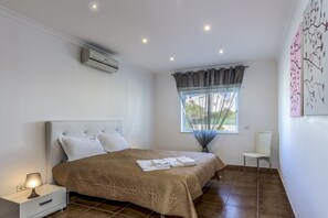 A bedroom with a bed, a nightstand, a chair, a window with curtains, and wall art.