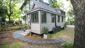 A small, single-story house with a porch, surrounded by a garden and trees.