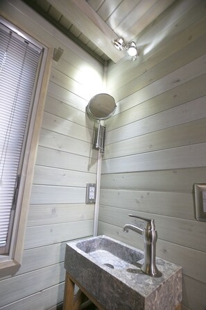 A bathroom with a wooden wall, a window with blinds, a sink with a marble countertop, and a handheld showerhead. - South Congress Tiny House Jewel! (Austin)