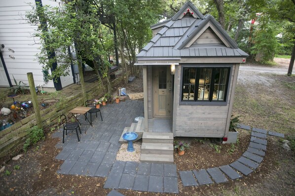 A small wooden structure with a sloped roof, a door, and a window. It is surrounded by a paved patio with a blue bowl and potted plants. - South Congress Tiny House Jewel! (Austin)