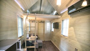 A compact room with a bunk bed, a small seating area, a ladder, and a television mounted on the wall.