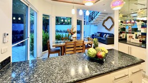 A modern kitchen with a granite countertop, a dining area with a glass table, and a living area with a sofa and a staircase. - Two Adjacent Gated Partial Ocean View Villas (Tamarindo)