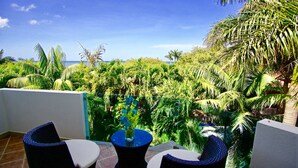 A balcony with two wicker chairs, a small table with a vase, and a view of the ocean and tropical vegetation. - Two Adjacent Gated Partial Ocean View Villas (Tamarindo)