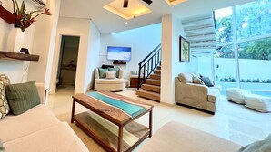 A modern living room with a wooden coffee table, a sofa, a TV mounted on the wall, and a staircase leading to another level. - Two Adjacent Gated Partial Ocean View Villas (Tamarindo)