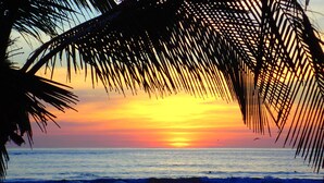 A beach scene with a sunset, palm trees, and a couple walking on the sand. - Two Adjacent Gated Partial Ocean View Villas (Tamarindo)