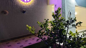 A modern building exterior with a circular light fixture on the wall, potted plants, and a textured wall surface. - Ville Ninfea - 2 independent twin pool villas, 150 mt by the sea Fontane Bianche (Fontane Bianche)