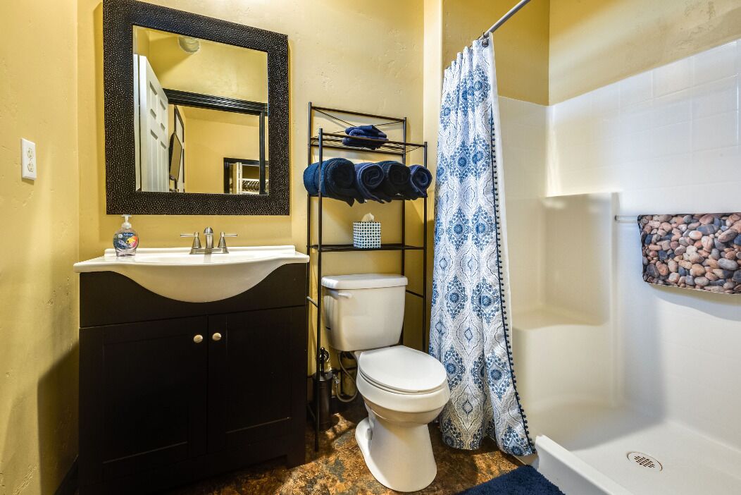 A bathroom with a sink, toilet, and shower. There is a mirror above the sink and a towel rack with towels.