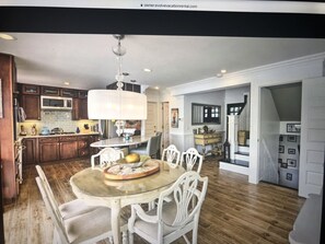 Una cocina amplia con armarios de madera, un comedor con mesa de vidrio, y una escalera que sube a otro nivel.