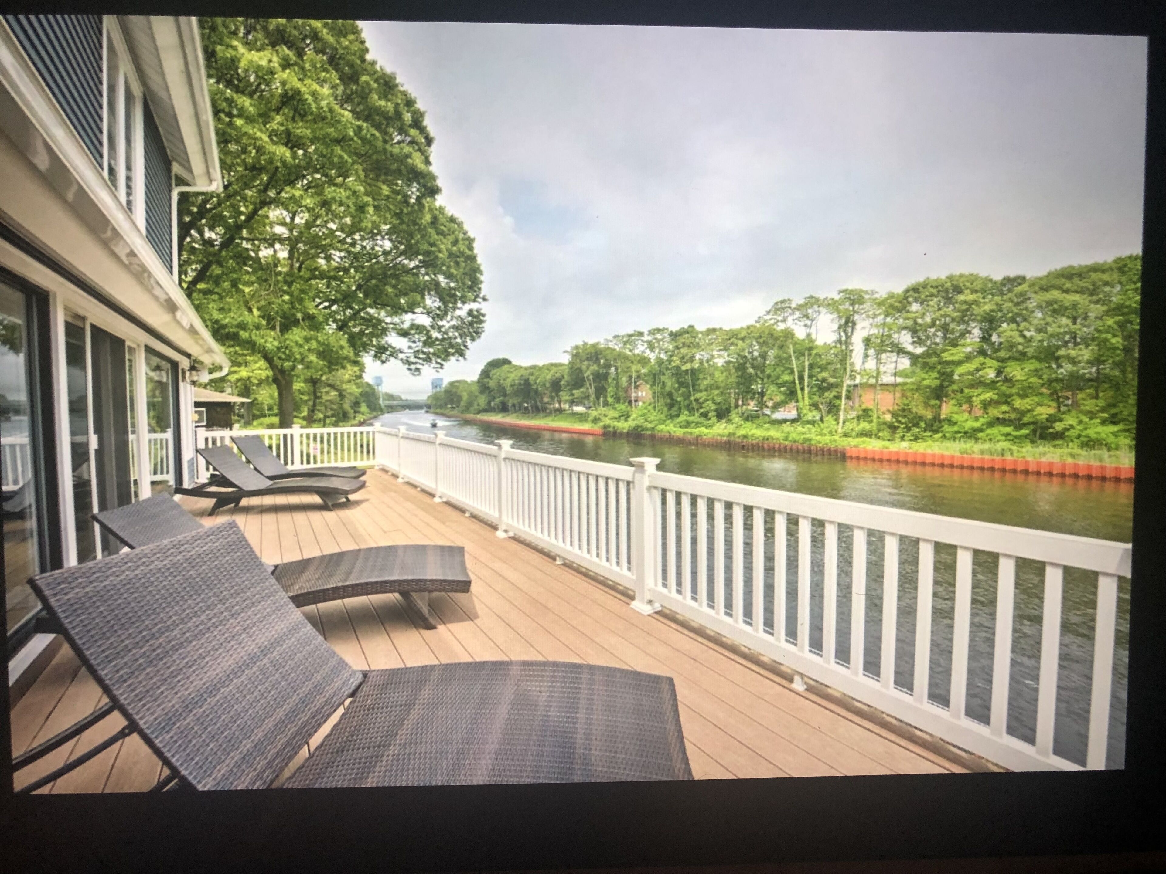 A deck with lounge chairs overlooking a river, surrounded by greenery and a white railing.