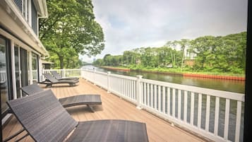 A deck with lounge chairs overlooking a river, surrounded by greenery and a white railing.