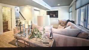 A living room with a sofa, a coffee table with candles, a lamp, and a TV mounted on the wall.