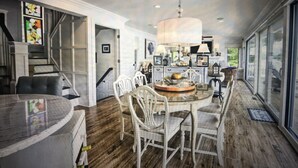 A spacious dining area with a large table and chairs, a chandelier, and a view through the glass doors.