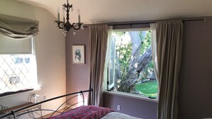 A bedroom with a bed, a window with curtains, a chandelier, and a picture on the wall.