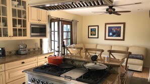 A kitchen with a stove, cabinets, a microwave, and a dining area with a sofa and chairs.