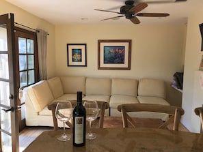A cozy living room with a beige sofa, a wooden table with a wine bottle, two wine glasses, and a ceiling fan.