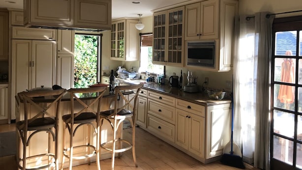 A kitchen with wooden cabinets, a ceiling fan, and a window with curtains.