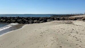 A sandy beach with a rocky breakwater and a clear blue sky. - Late August and fall dates available! (Dennis)