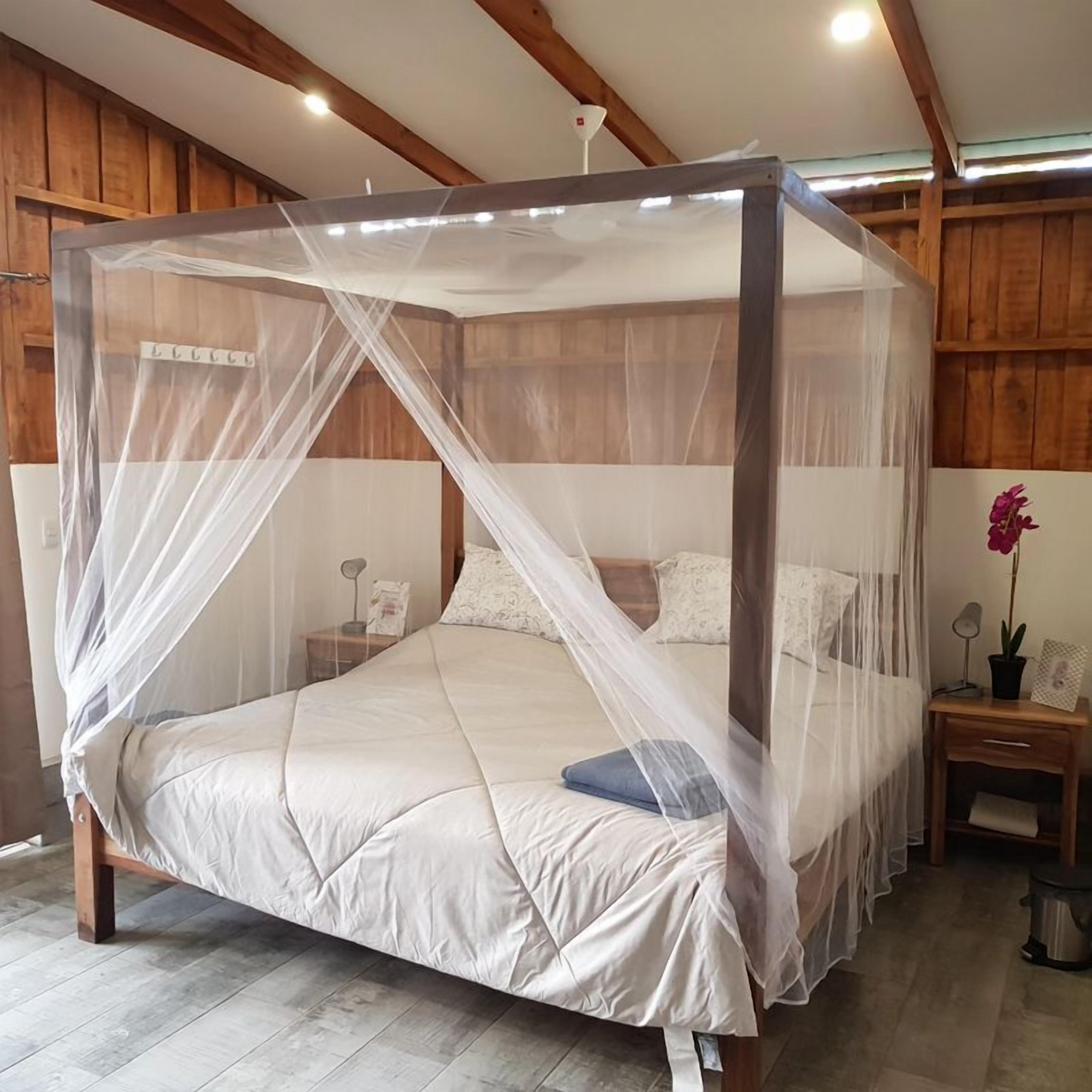 A four-poster canopy bed with a white bedspread and pillows, wooden headboard, and nightstands with lamps and a potted plant.
