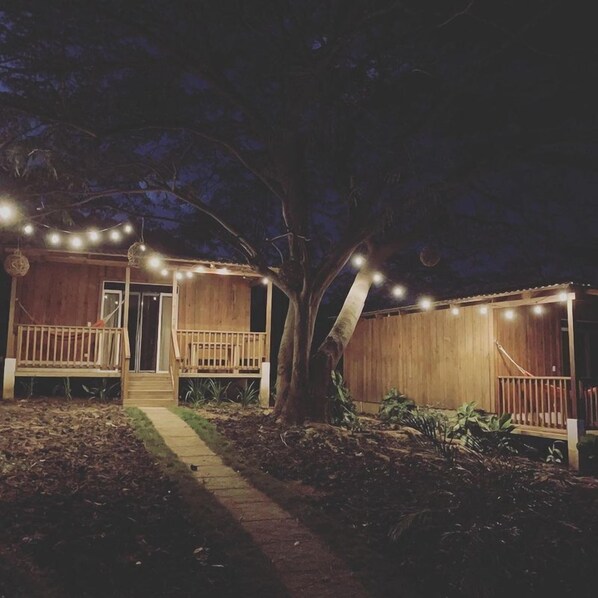 A wooden cabin with a porch and string lights, surrounded by trees. - Calalas Lodge (Nindiri)