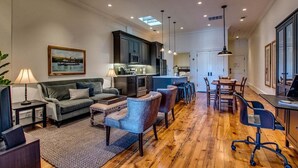 A spacious living area with a sofa, chairs, a coffee table, and a dining table with chairs. There is a kitchen area with cabinets and a countertop.