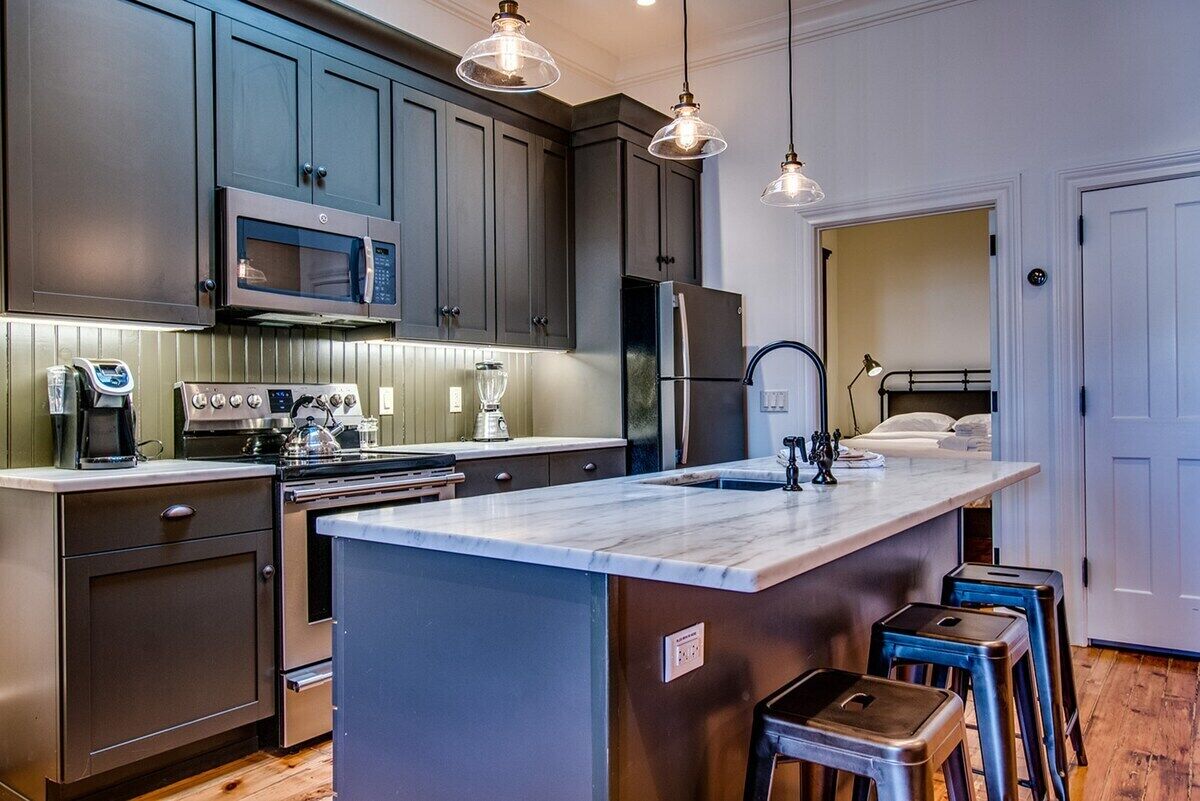 A modern kitchen with dark cabinets, stainless steel appliances, and a marble island with bar stools.