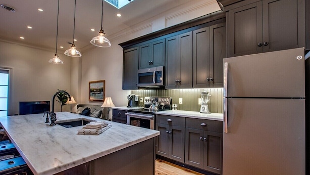 A modern kitchen with dark cabinets, a large island, a microwave, and a refrigerator.
