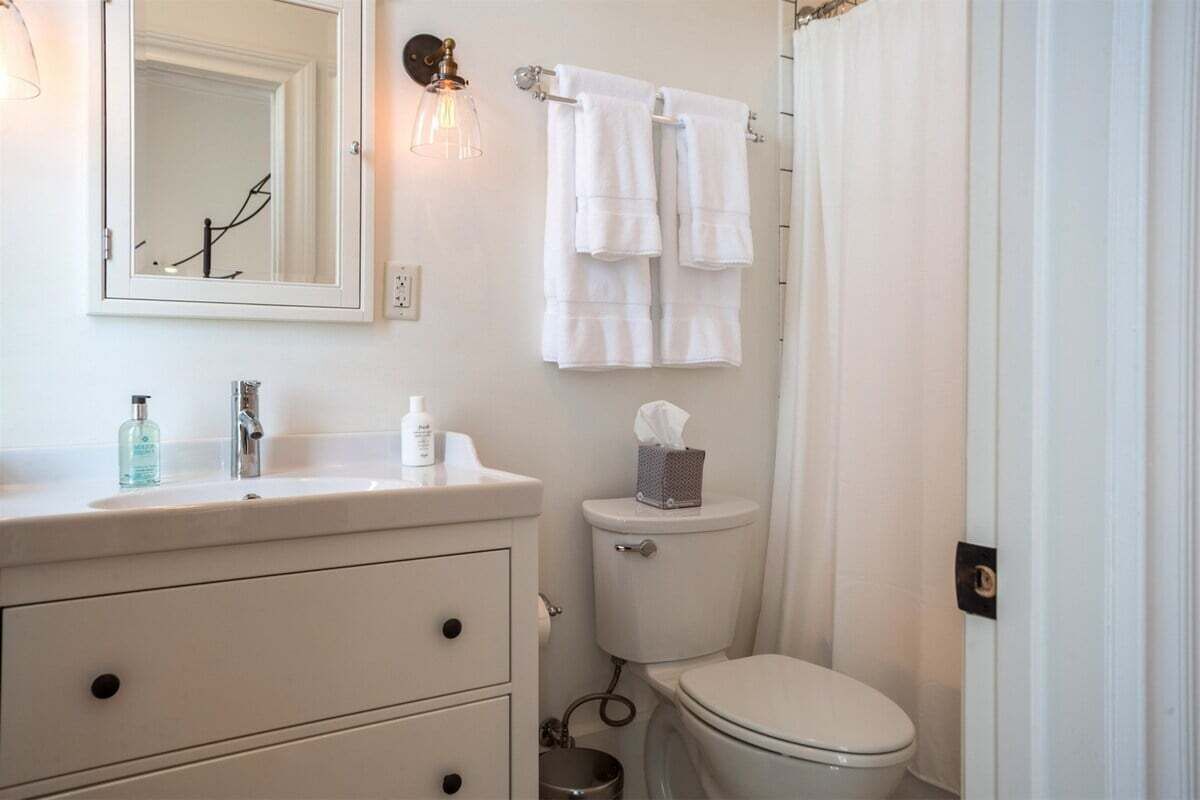 A bathroom with a white sink, mirror, and toilet. There are towels hanging on a rack, a tissue box, and a soap dispenser on the sink.