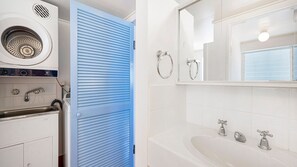 A modern bathroom with a built-in washing machine, a bathtub, and a large mirror.