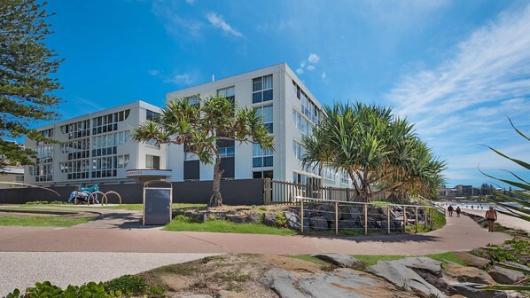 A modern building with a flat roof, large windows, and a paved walkway leading to a beach.