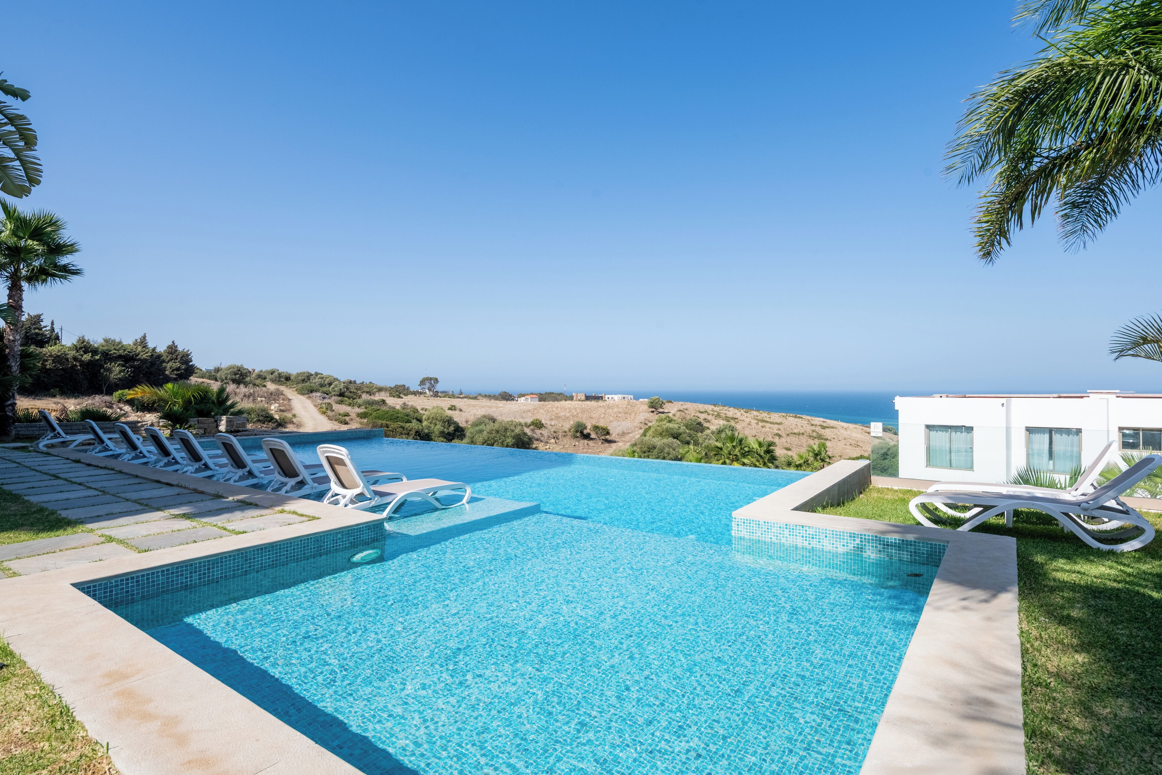 A swimming pool with lounge chairs, a view of the ocean, and a modern building in the background.
