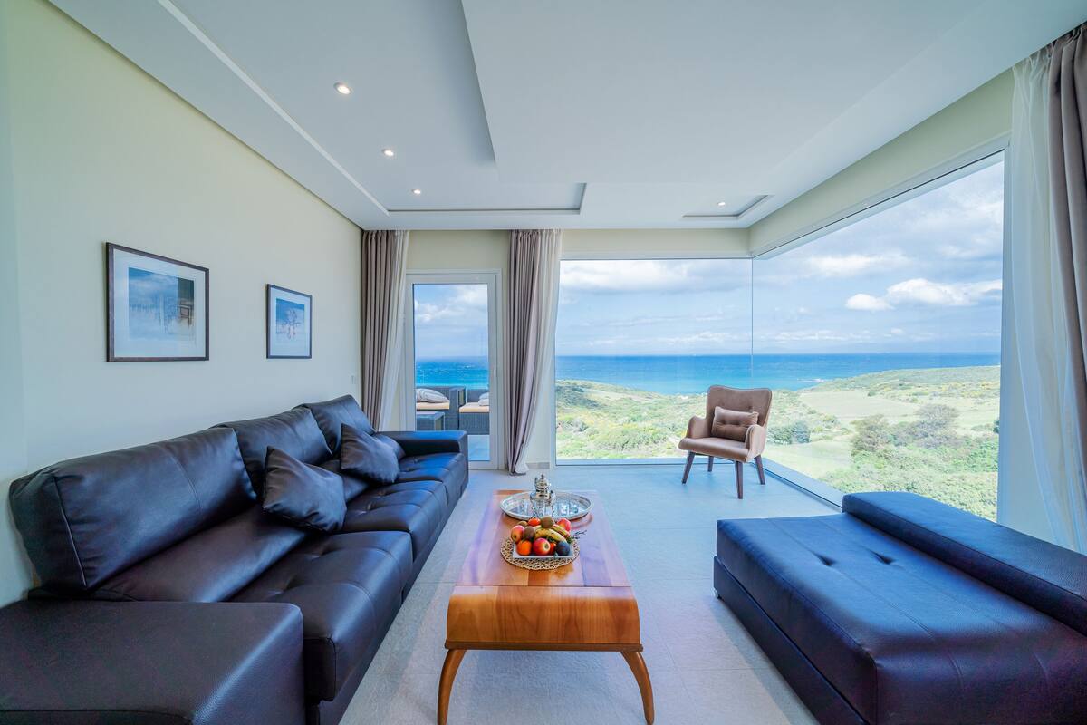 Una sala de estar moderna con un sofá, una mesa de centro con fruta y vistas al mar.