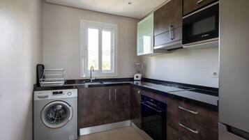 A compact kitchen with a washing machine, oven, microwave, and a window providing natural light.