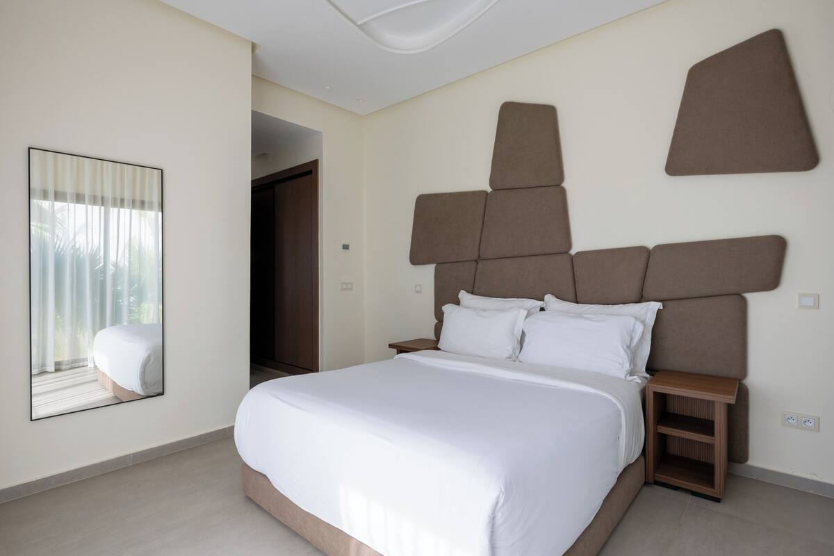 Habitación de hotel moderna con una cama grande, una mesita de noche, un espejo y vistas a un balcón.