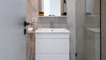 Moderni kylpyhuone, jossa on suuri peili, valkoinen allaskaappi ja lasinen suihkuseinä.