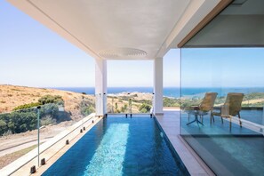 Une piscine à débordement moderne, avec une eau d’un bleu cristallin, de grandes fenêtres et une vue sur l’océan.