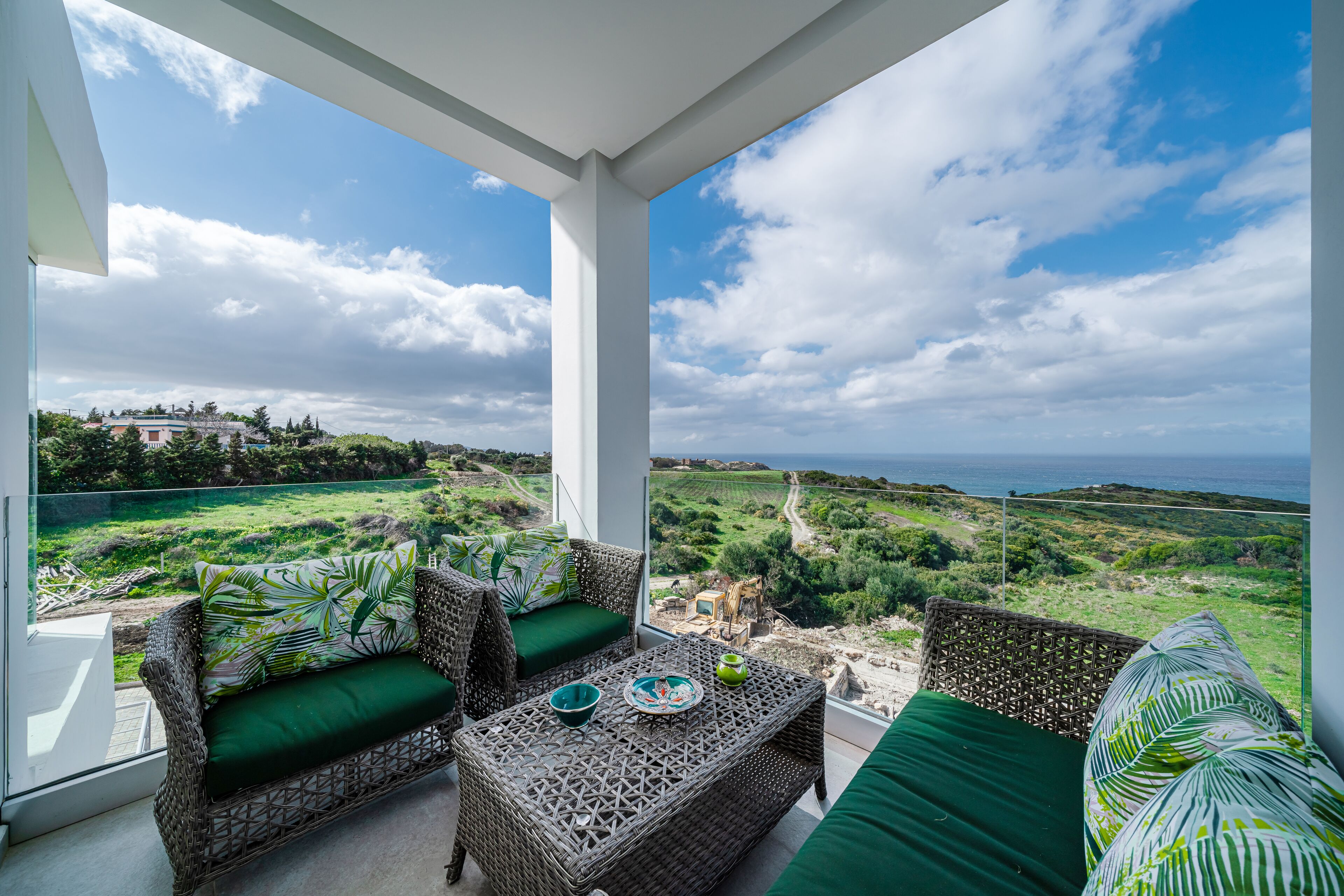 A balcony with wicker furniture, a view of a coastal landscape, and a clear sky.