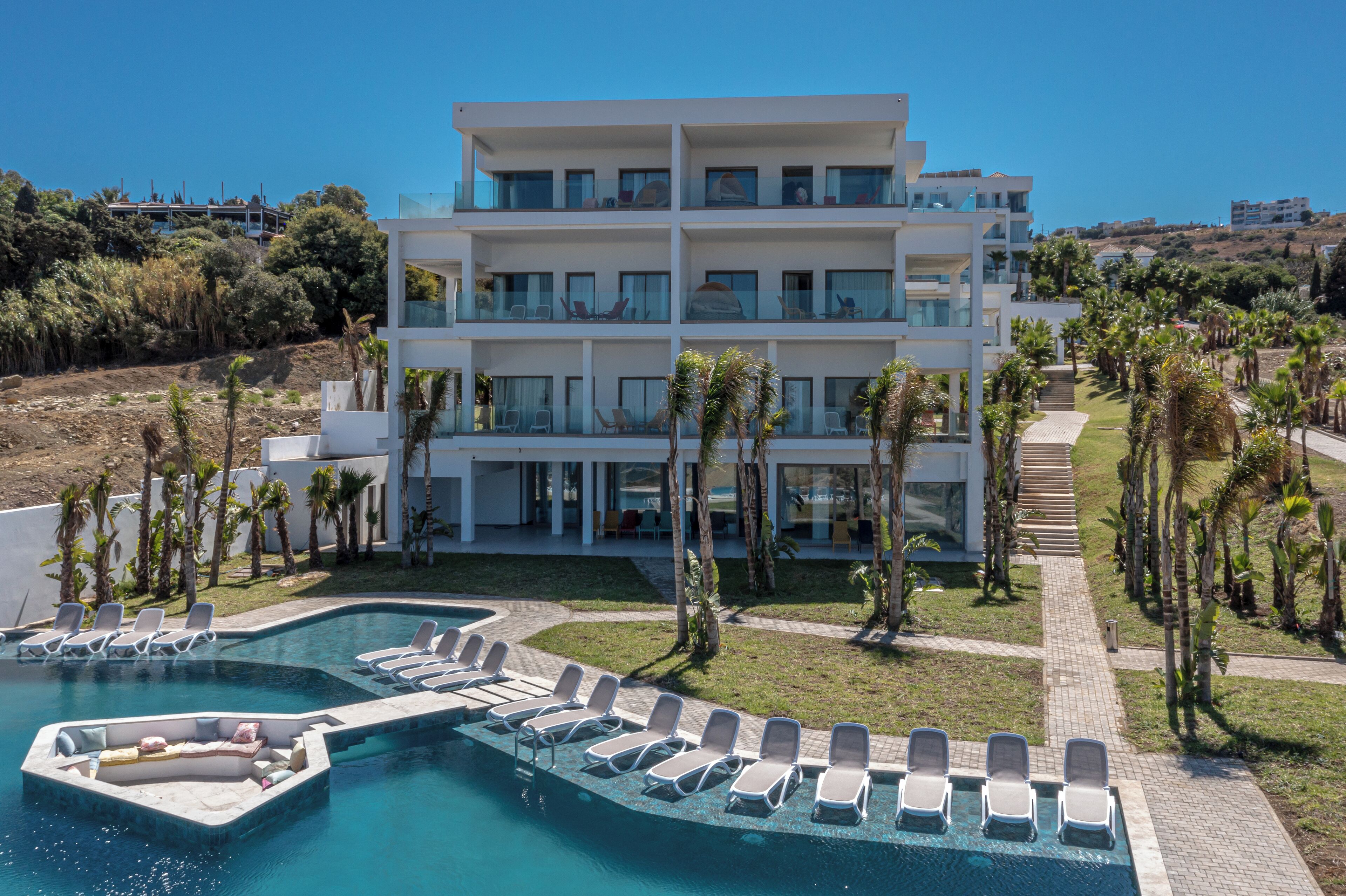 A modern multi-story hotel with a swimming pool and sun loungers.
