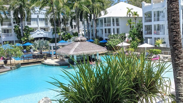 Un complexe hôtelier doté d’une piscine entourée de palmiers et de chaises longues.
