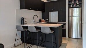 Une cuisine moderne dotée d’un îlot central, de meubles noirs, d’appareils électroménagers en acier inoxydable et de tabourets de bar.
